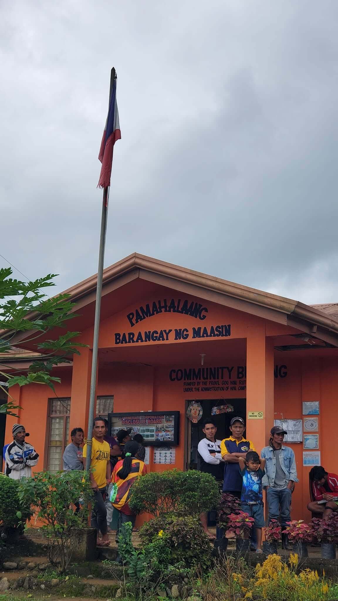 The orange Pamahalaang Barangay ng Maasin community building with Philippine flag, community members gathered outside on distribution day, Quezon, Nueva Vizcaya